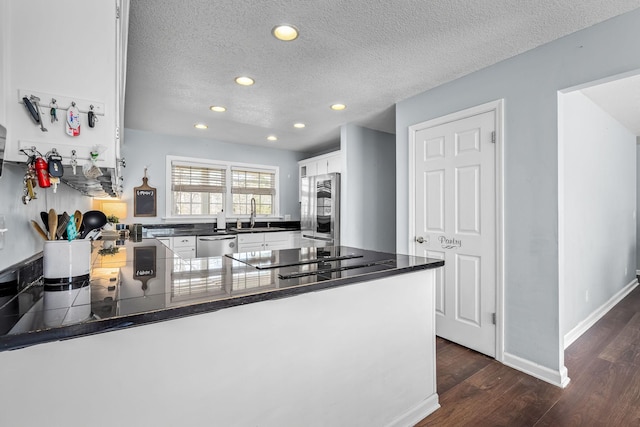 kitchen with dark wood-type flooring, sink, appliances with stainless steel finishes, kitchen peninsula, and white cabinets