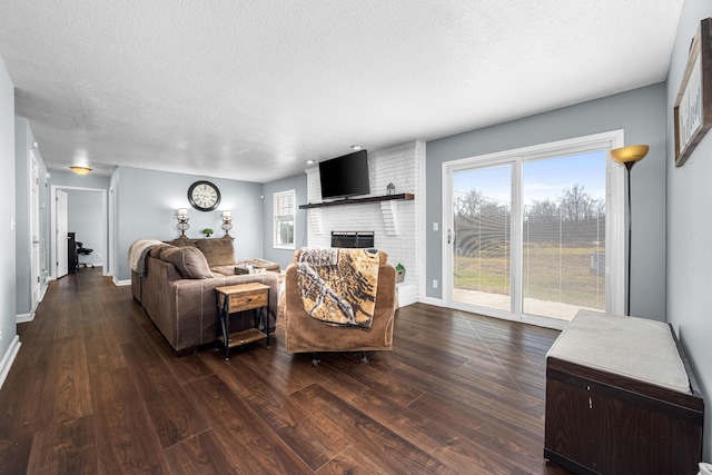 living room with a brick fireplace, dark wood-type flooring, a wealth of natural light, and a textured ceiling