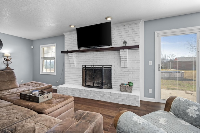 living room with dark wood-type flooring, a brick fireplace, and a textured ceiling