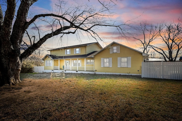 back house at dusk featuring a porch and a lawn