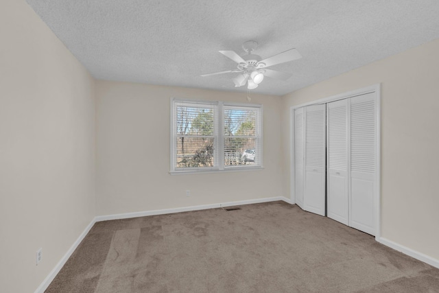 unfurnished bedroom featuring ceiling fan, light colored carpet, a closet, and a textured ceiling