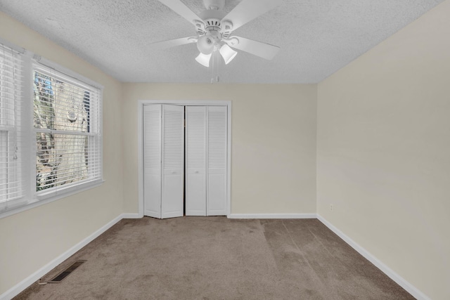 unfurnished bedroom featuring ceiling fan, a closet, light carpet, and a textured ceiling