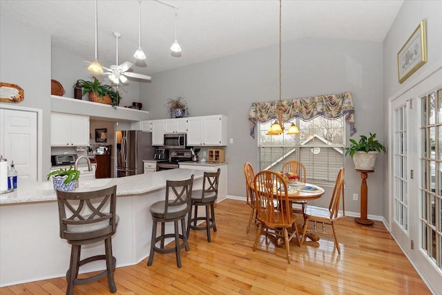 kitchen featuring white cabinetry, decorative light fixtures, stainless steel appliances, and a breakfast bar