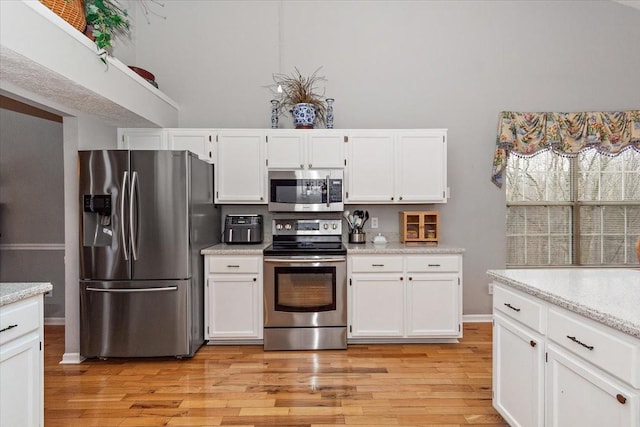 kitchen featuring white cabinetry, appliances with stainless steel finishes, light stone counters, and light wood-type flooring