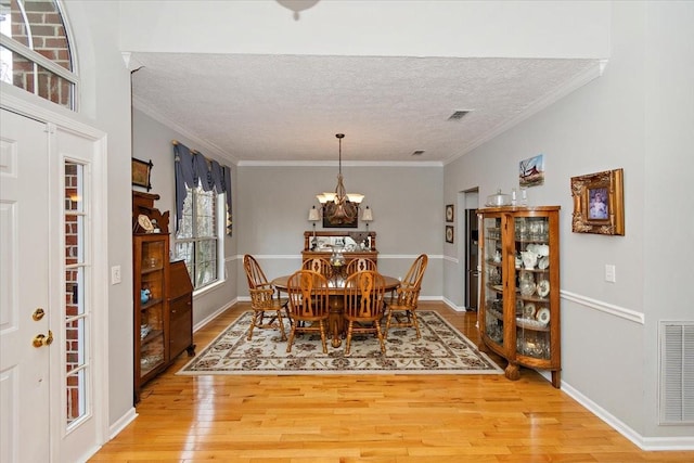 dining room with an inviting chandelier, light hardwood / wood-style flooring, ornamental molding, and a textured ceiling