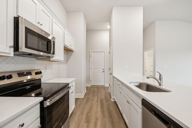 kitchen with sink, white cabinetry, stainless steel appliances, light hardwood / wood-style floors, and decorative backsplash