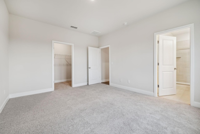 unfurnished bedroom with a walk in closet, connected bathroom, a closet, and light carpet