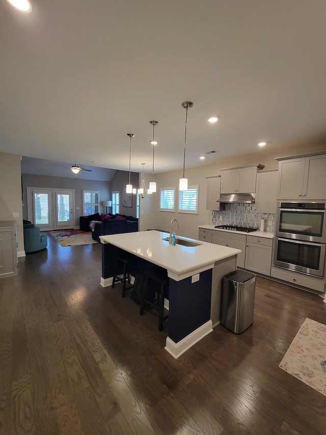 kitchen with sink, gas stovetop, dark hardwood / wood-style floors, stainless steel double oven, and a kitchen island with sink