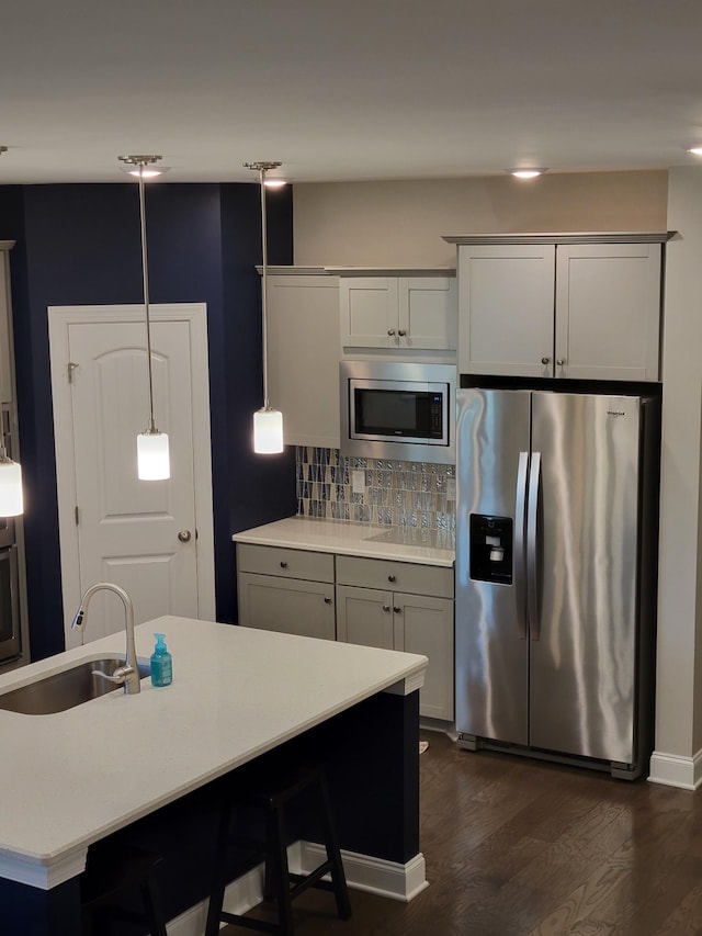 kitchen with sink, hanging light fixtures, an island with sink, stainless steel appliances, and decorative backsplash