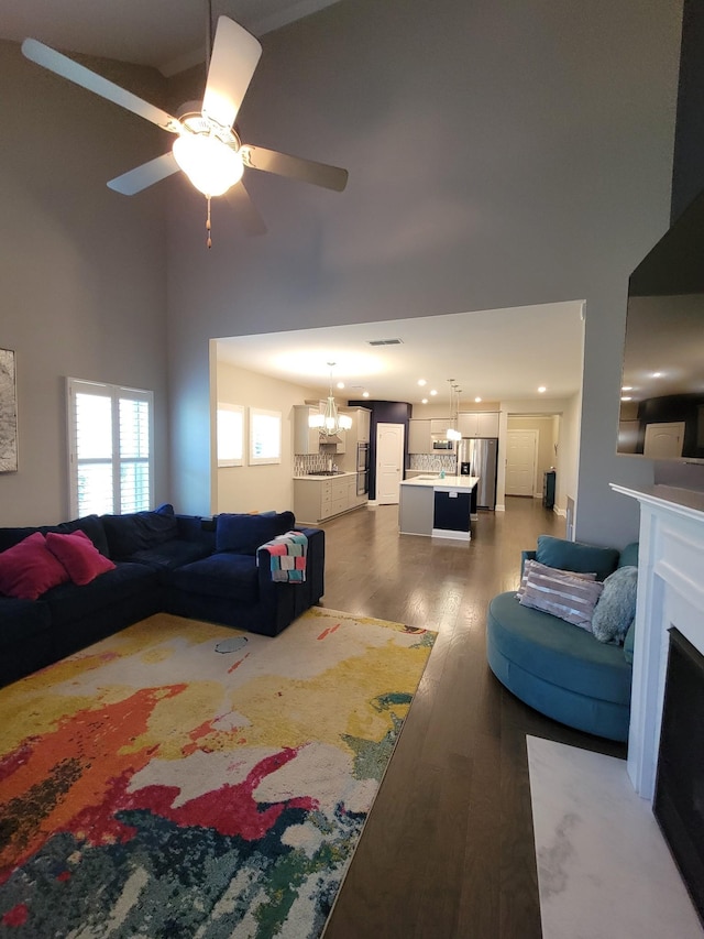 living room with dark hardwood / wood-style floors, ceiling fan with notable chandelier, and a high ceiling