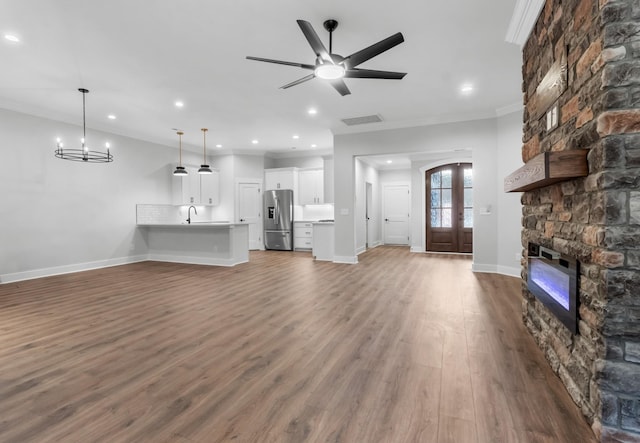 unfurnished living room featuring sink, crown molding, ceiling fan with notable chandelier, dark hardwood / wood-style floors, and a stone fireplace