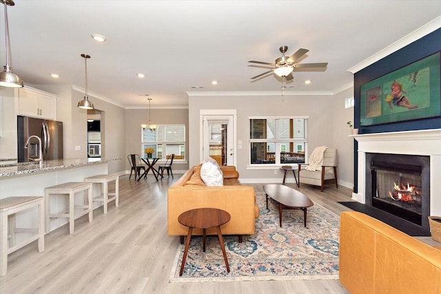 living room featuring sink, ceiling fan with notable chandelier, ornamental molding, and light wood-type flooring