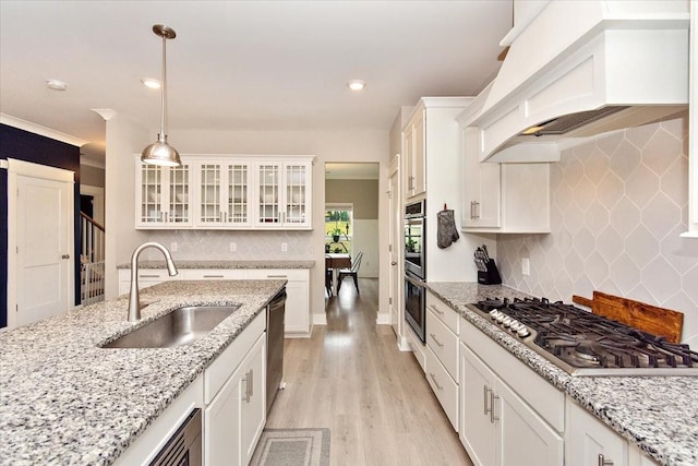 kitchen with pendant lighting, sink, white cabinets, custom exhaust hood, and stainless steel appliances