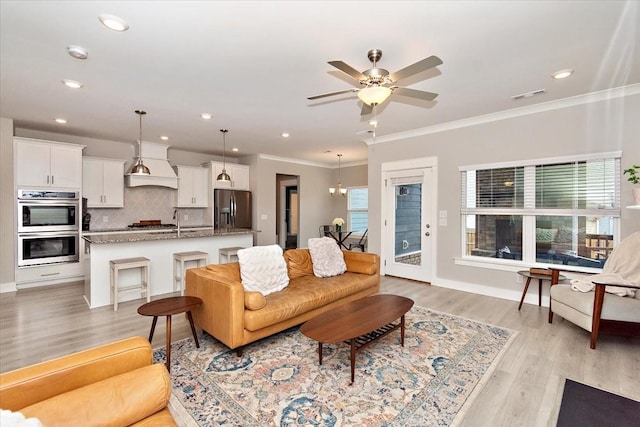 living room featuring crown molding, sink, ceiling fan with notable chandelier, and light hardwood / wood-style flooring