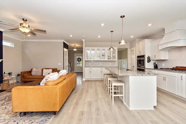 kitchen featuring pendant lighting, light stone counters, a center island with sink, and white cabinets