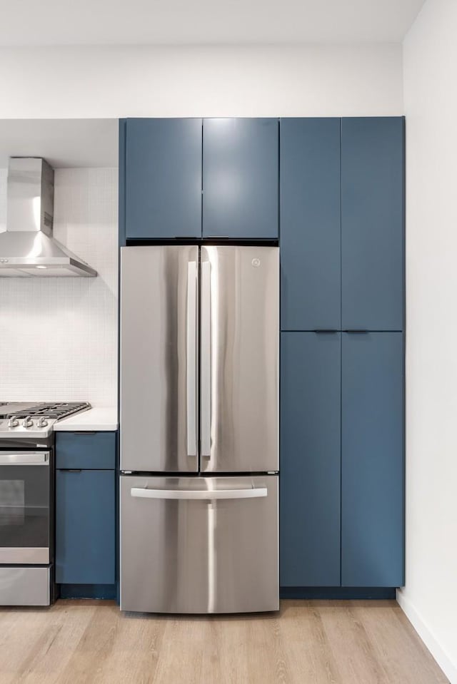 kitchen with blue cabinets, light hardwood / wood-style floors, wall chimney exhaust hood, and appliances with stainless steel finishes