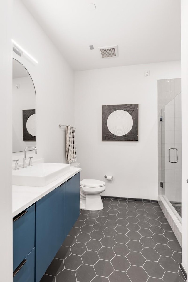 bathroom featuring tile patterned flooring, vanity, toilet, and a shower with shower door