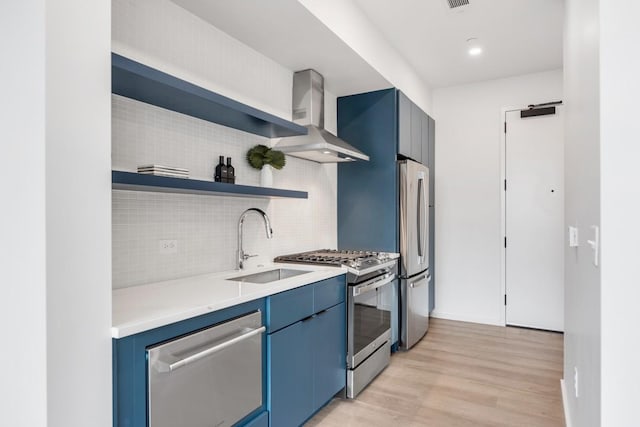 kitchen featuring backsplash, wall chimney exhaust hood, stainless steel appliances, blue cabinetry, and light hardwood / wood-style flooring