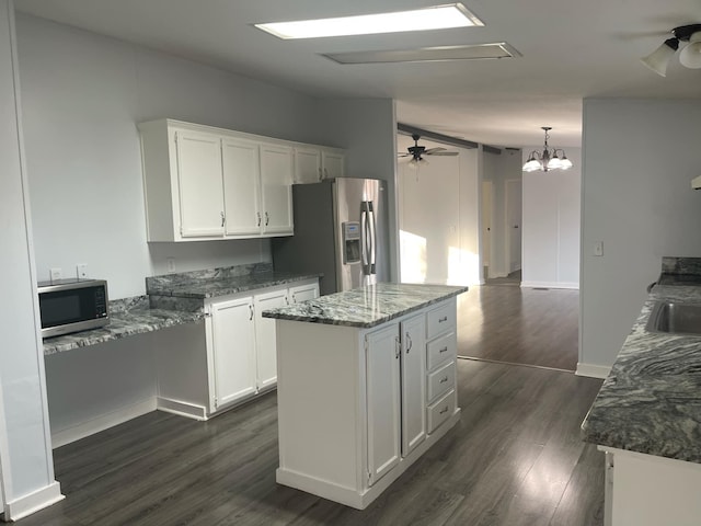 kitchen featuring ceiling fan, white cabinetry, stainless steel appliances, a center island, and dark stone counters