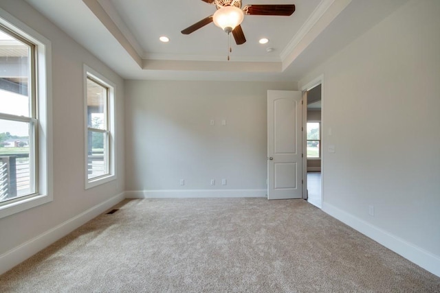 unfurnished room featuring a raised ceiling, ornamental molding, light colored carpet, and ceiling fan