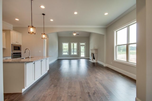 kitchen with a kitchen island with sink, hanging light fixtures, stainless steel appliances, light stone countertops, and white cabinets