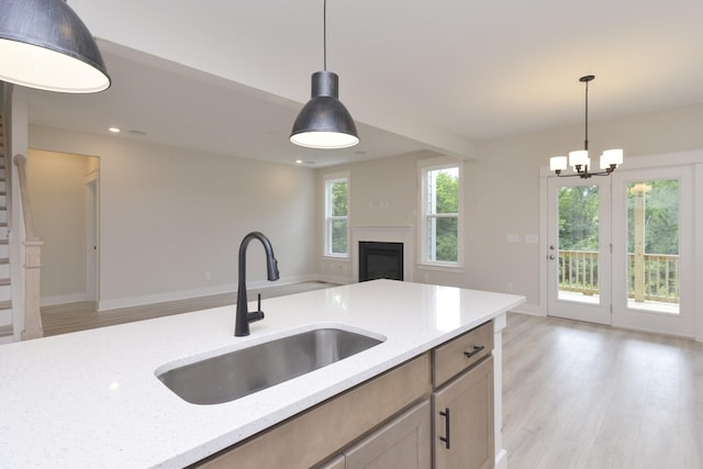 kitchen featuring pendant lighting, light stone countertops, sink, and light wood-type flooring