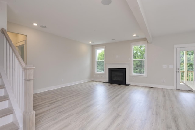 unfurnished living room with beam ceiling, light hardwood / wood-style flooring, and a healthy amount of sunlight