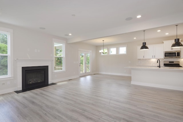 unfurnished living room featuring an inviting chandelier, plenty of natural light, sink, and light hardwood / wood-style flooring