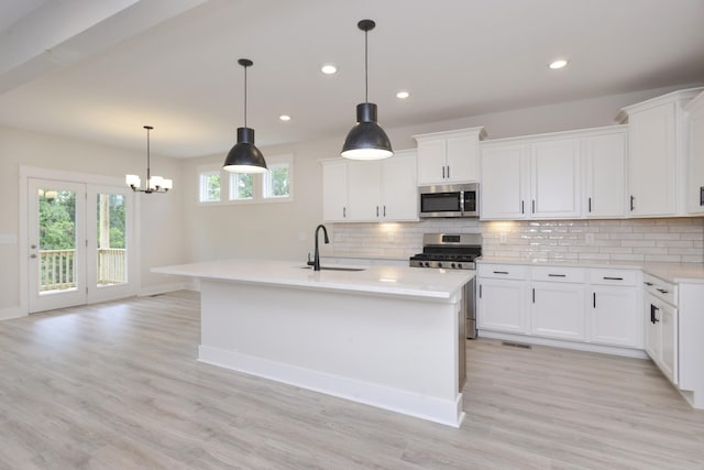 kitchen with stainless steel appliances, white cabinetry, hanging light fixtures, and an island with sink