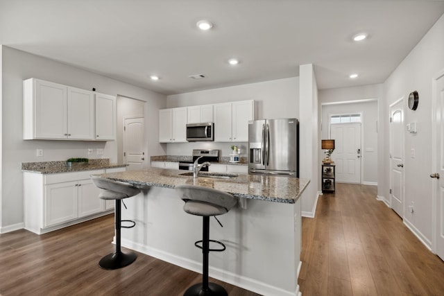 kitchen with appliances with stainless steel finishes, a kitchen breakfast bar, light stone counters, white cabinets, and a center island with sink