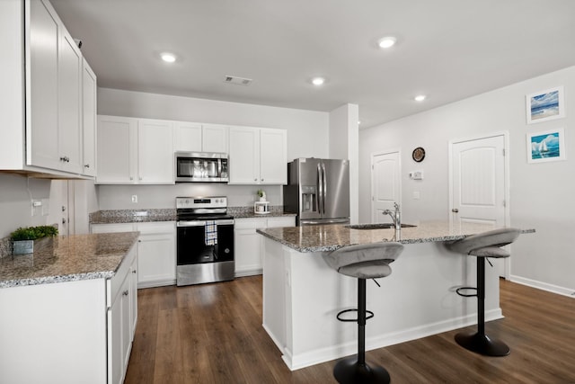 kitchen featuring stone countertops, an island with sink, sink, white cabinets, and stainless steel appliances