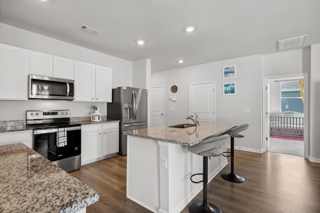 kitchen featuring white cabinetry, light stone counters, a center island with sink, and appliances with stainless steel finishes