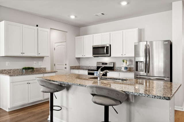 kitchen featuring an island with sink, appliances with stainless steel finishes, white cabinets, and a kitchen bar