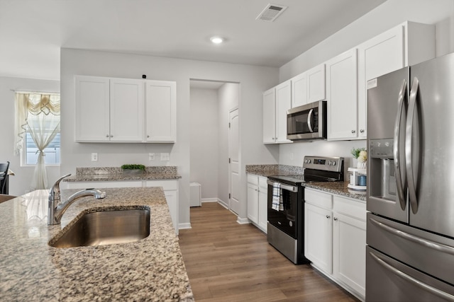 kitchen with stainless steel appliances, white cabinetry, sink, and light stone counters