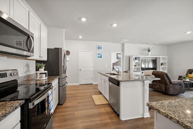 kitchen featuring a center island with sink, appliances with stainless steel finishes, stone counters, hardwood / wood-style flooring, and white cabinets