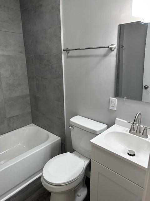 full bathroom with tiled shower / bath combo, vanity, hardwood / wood-style floors, and toilet