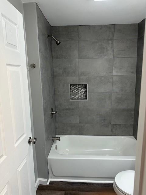 bathroom with tiled shower / bath combo, wood-type flooring, and toilet