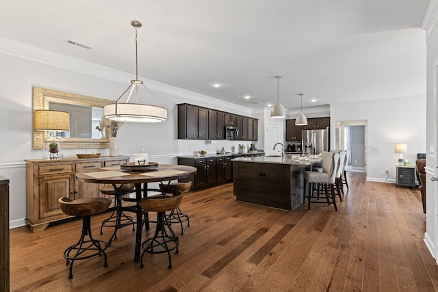 kitchen with appliances with stainless steel finishes, a breakfast bar, a center island with sink, and pendant lighting