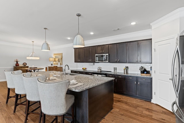 kitchen featuring appliances with stainless steel finishes, decorative light fixtures, sink, and a center island with sink