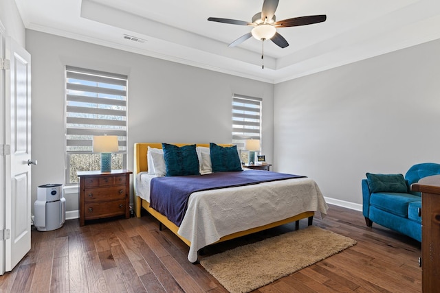 bedroom featuring dark wood-type flooring, ornamental molding, a raised ceiling, and ceiling fan