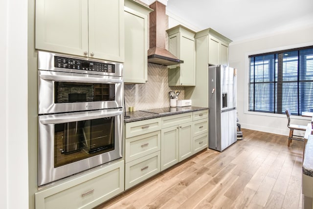 kitchen with tasteful backsplash, light wood-type flooring, appliances with stainless steel finishes, custom range hood, and dark stone counters