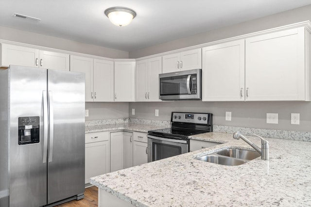 kitchen with sink, light stone counters, light hardwood / wood-style flooring, appliances with stainless steel finishes, and white cabinets