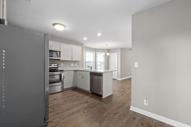 kitchen featuring pendant lighting, sink, appliances with stainless steel finishes, white cabinets, and kitchen peninsula