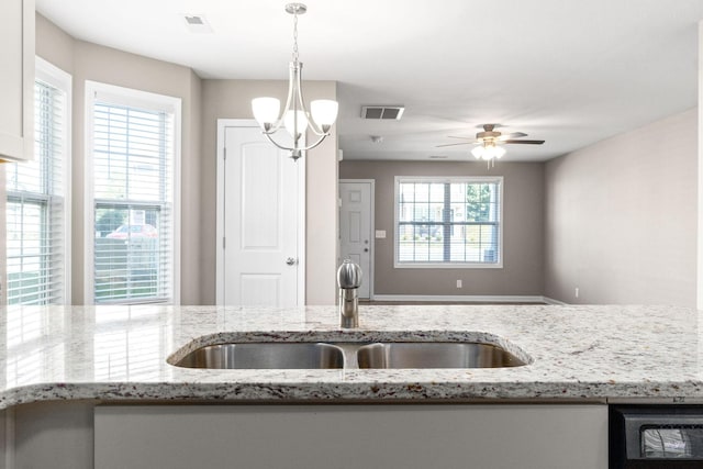 kitchen with light stone counters, hanging light fixtures, ceiling fan with notable chandelier, and sink