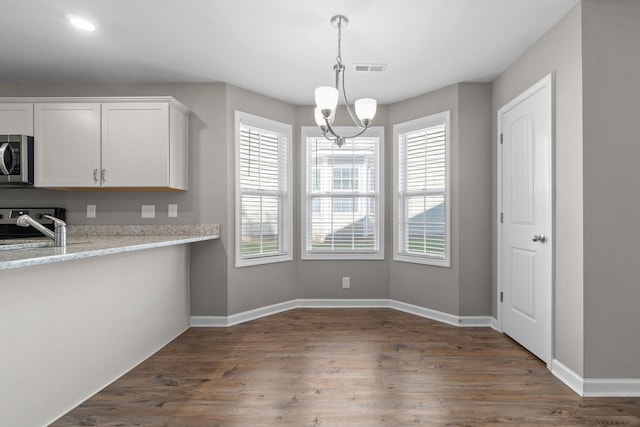 kitchen featuring white cabinetry, sink, hanging light fixtures, light stone counters, and dark wood-type flooring