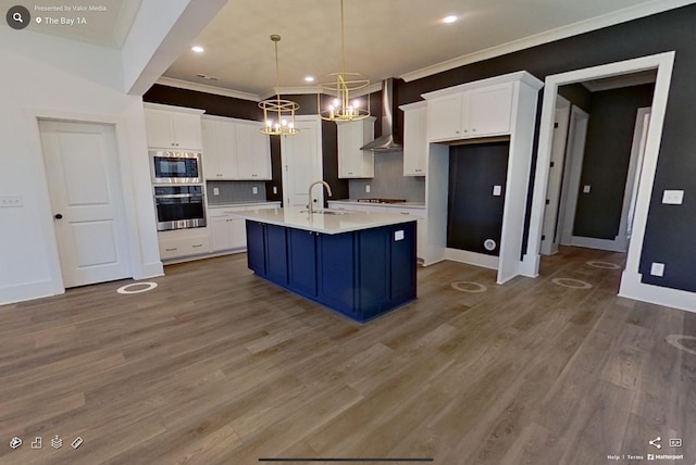 kitchen featuring stainless steel appliances, wood finished floors, a sink, white cabinets, and wall chimney range hood