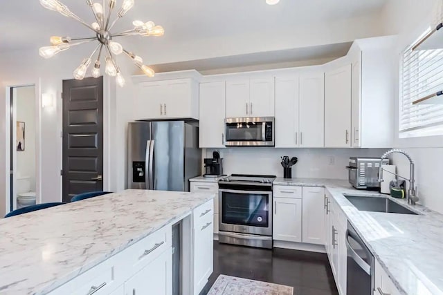 kitchen with sink, appliances with stainless steel finishes, white cabinetry, an inviting chandelier, and light stone countertops