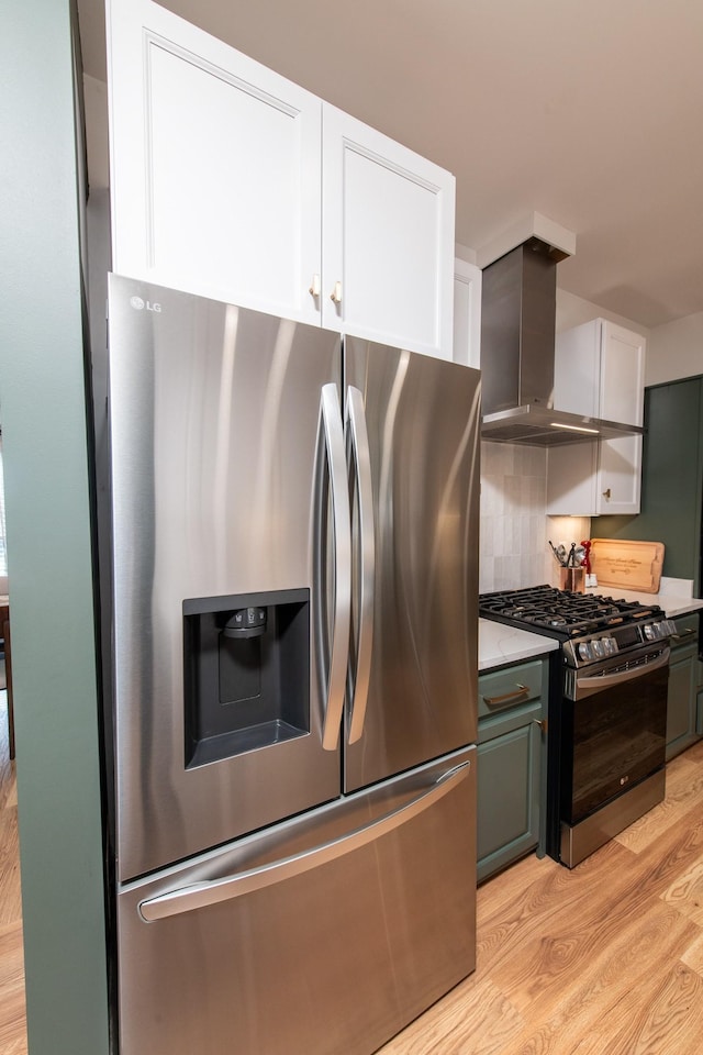 kitchen featuring white cabinetry, backsplash, stainless steel appliances, wall chimney range hood, and light hardwood / wood-style flooring