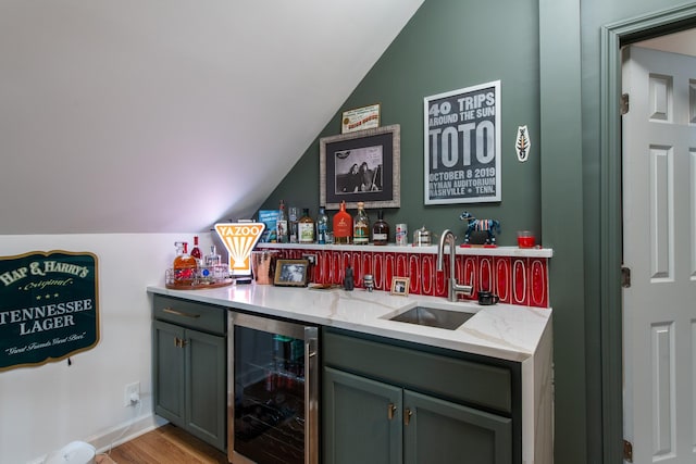 bar with vaulted ceiling, sink, wine cooler, light stone countertops, and light hardwood / wood-style flooring