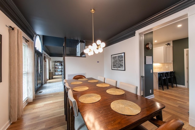 dining space featuring ornamental molding, light wood-type flooring, and an inviting chandelier